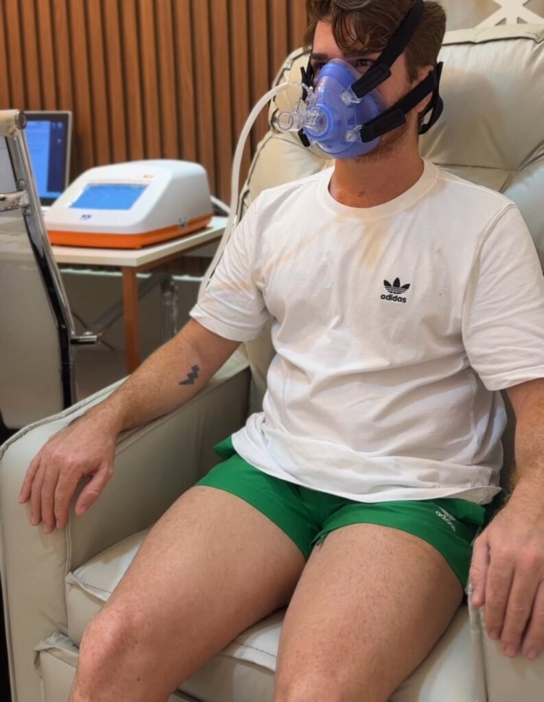 Paciente sentado durante a calorimetria indireta, com o aparelho ao fundo